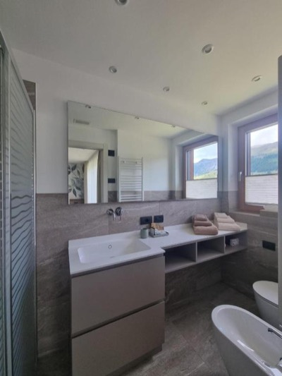 Bagno con lavabo sospeso, grande specchio e finestra affacciata sulle montagne