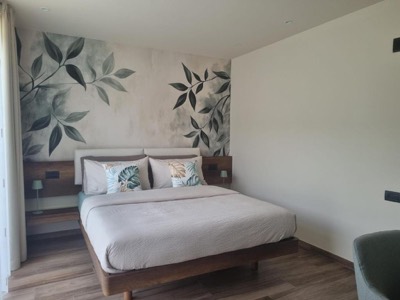 Letto matrimoniale con testiera in legno e parete decorata a foglie